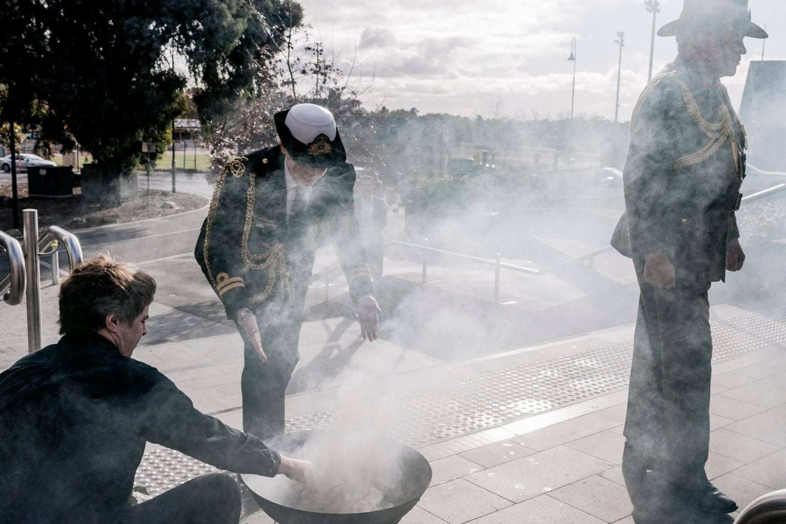 A person wearing an official uniform walks through smoke from a small fire pit.