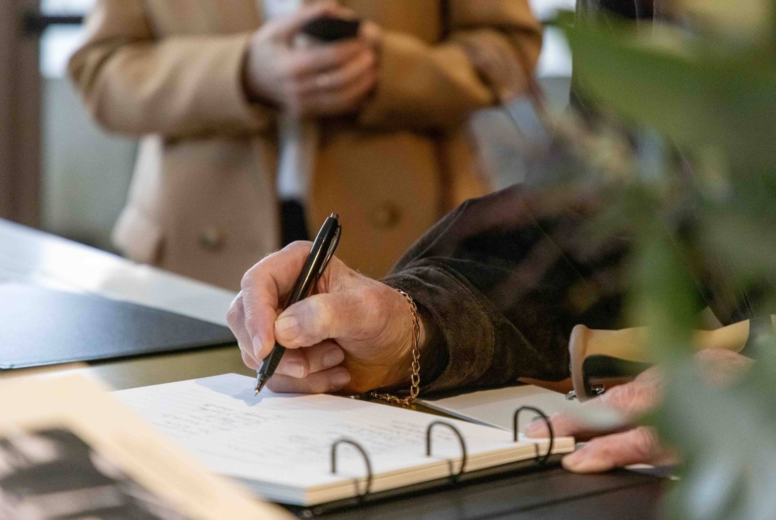 A hand holding a pen and signing a book.