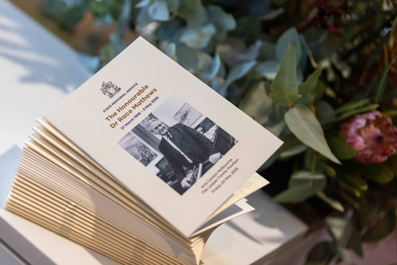 A pile of printed service programs with a photo of a man in a suit on the front. Flowers are in the background.