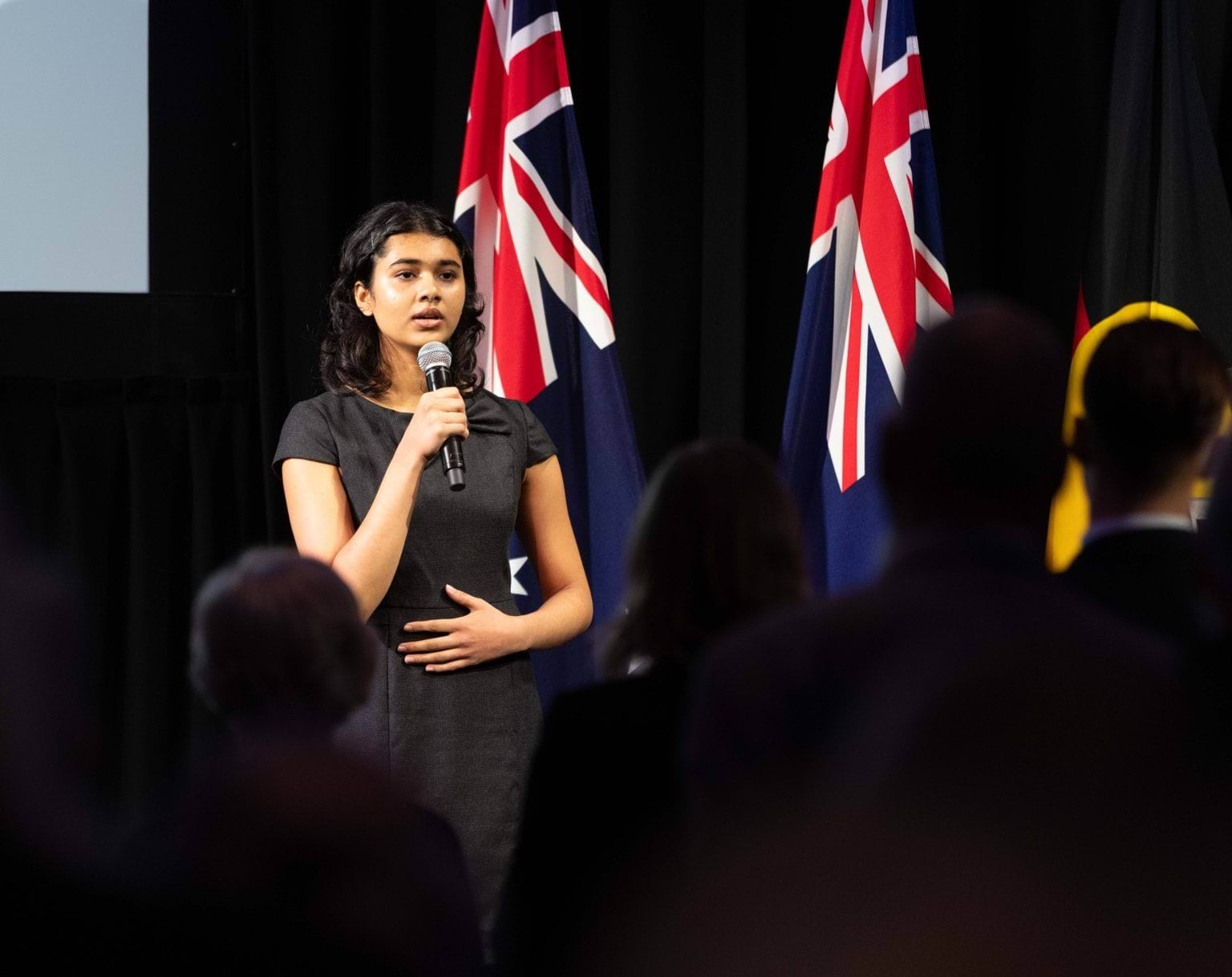 A person standing in front of Australian Flags while holding a microphone.