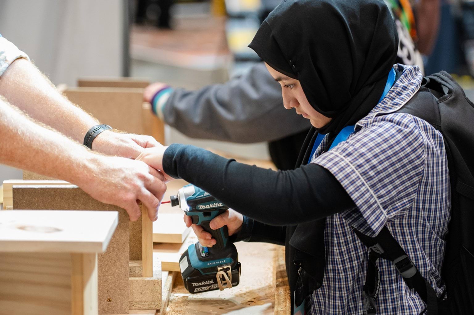 Female student drilling into wood with the support of an industry professional