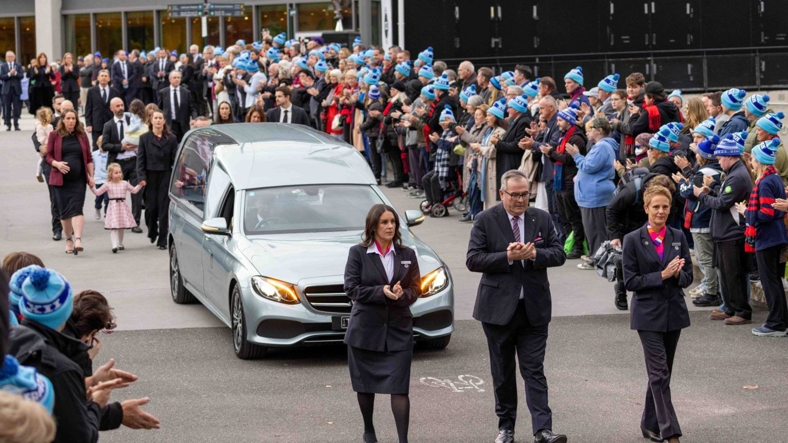 A guard of honour forms along Daniher's Way outside the MCG, with crowds applauding as the hearse passes them