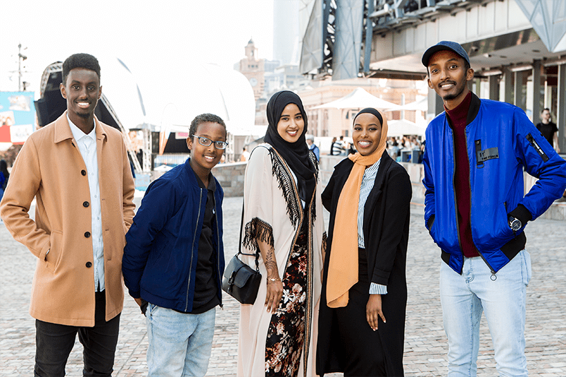 Five young people of African background stand together. Three males and two females.