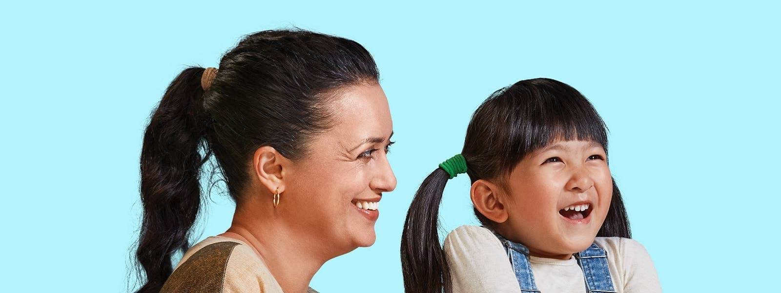 An early childhood professional and a young girl smile together, in front of a blue background.