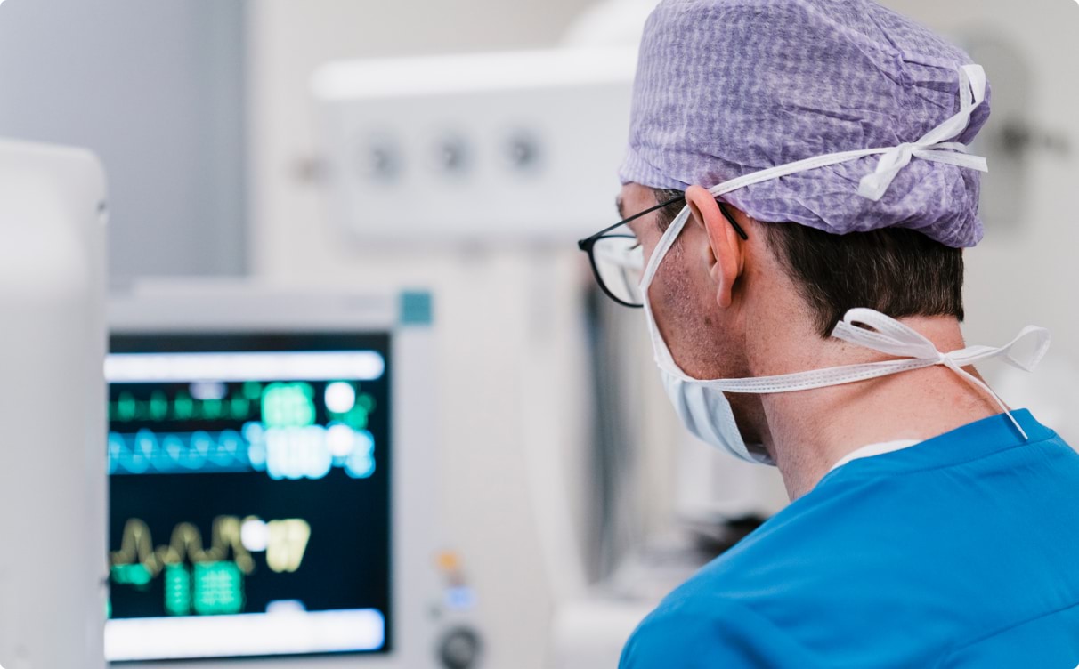 Man dressed in surgical scrubs looking at data on a monitor