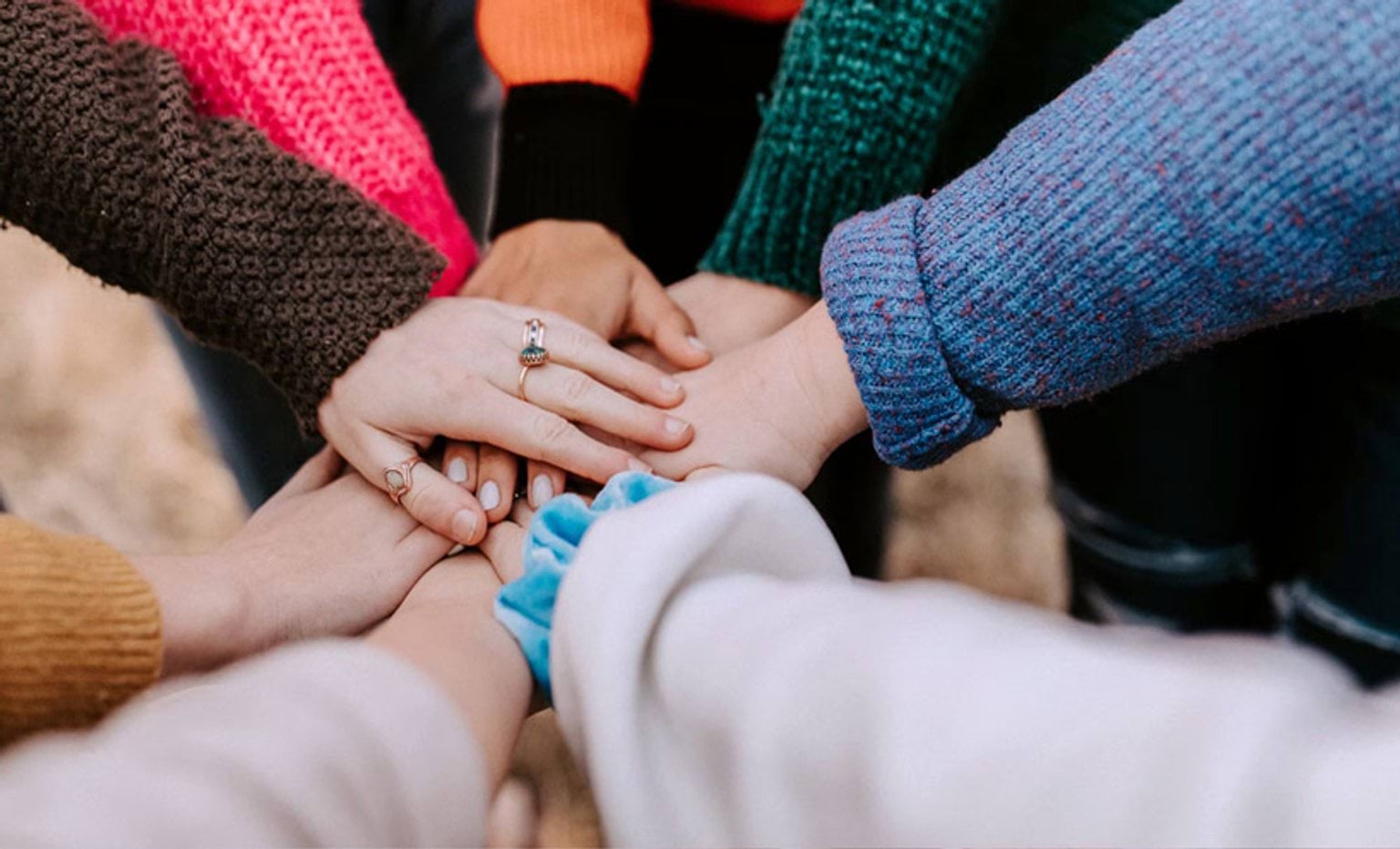 Group of people in a circle with their hands stacked together in the middle of a circle in solidarity