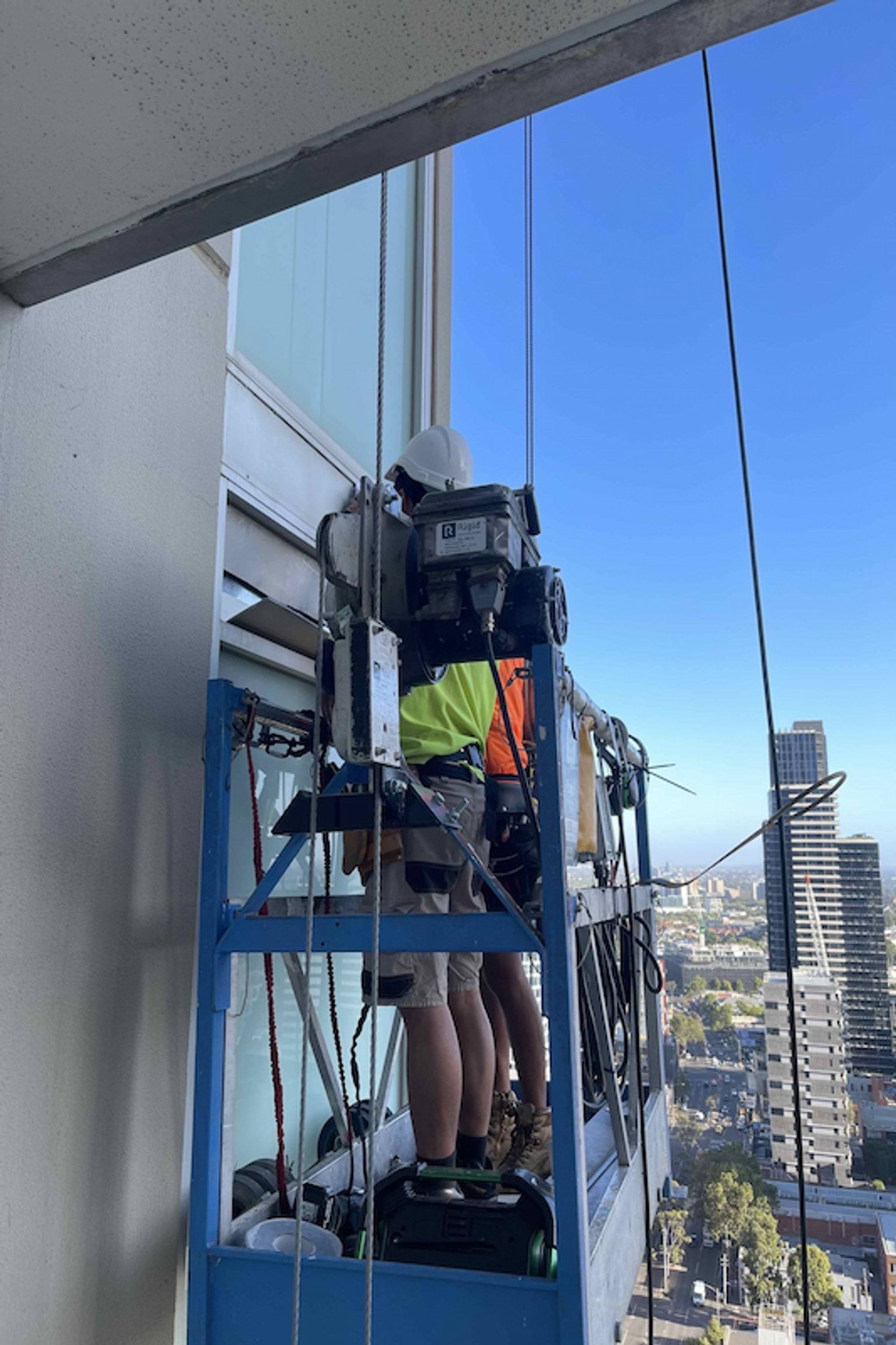 Close up of people working on a platform on the side of a high-rise building.