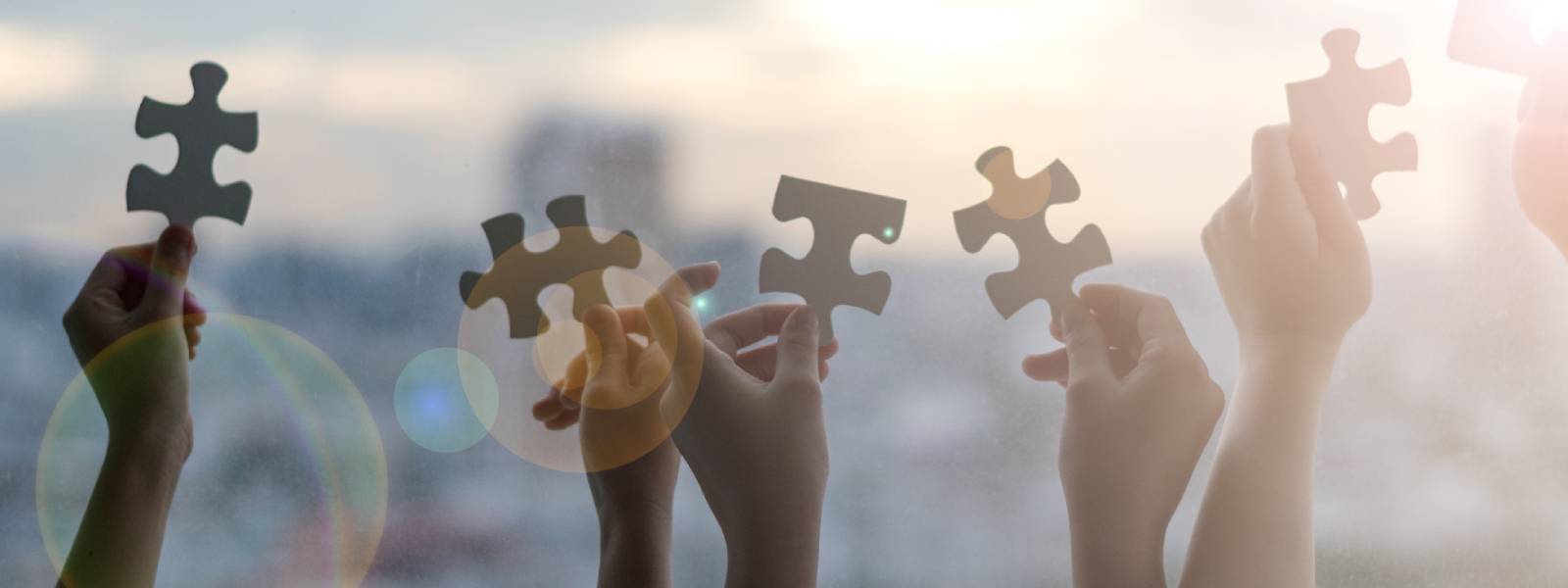 Hands holding jigsaw pieces up to a light