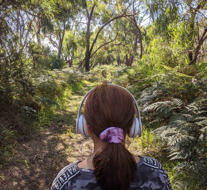 Back of the head photo of a person walking in bushland with headphones on