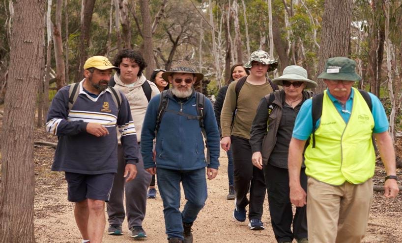 A group of people walking along a track in a park led by a volunteer guide.