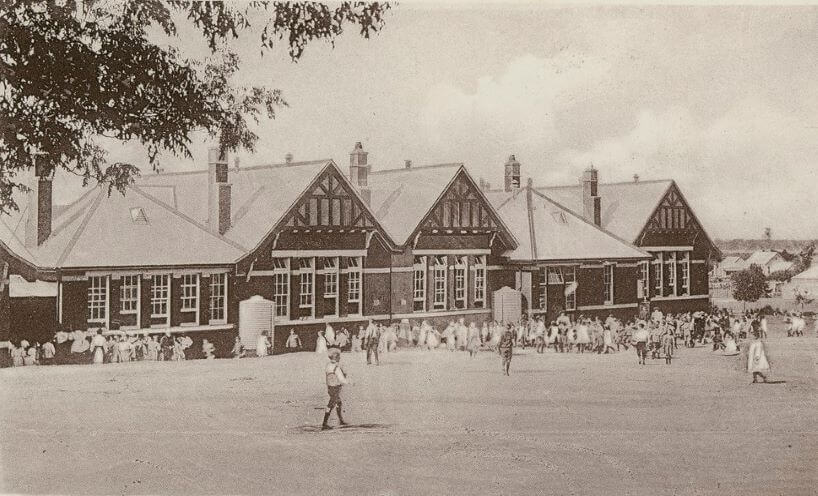 Black and white photograph of the Rutherglen school building with children playing in the yard in front of the school. 