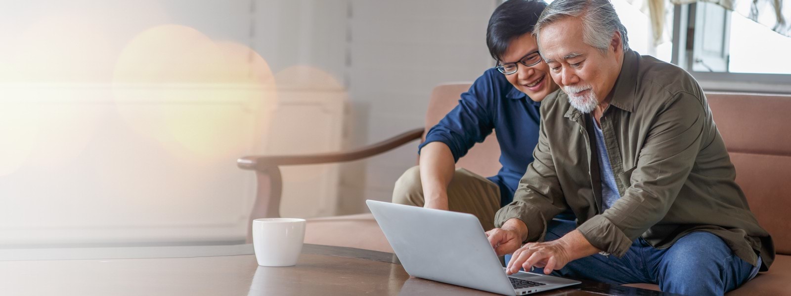 A senior person is using a laptop while a younger person watches