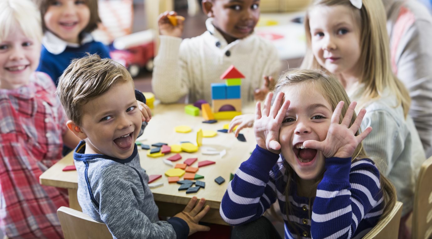 Young children sitting at a table smiling and making faces.