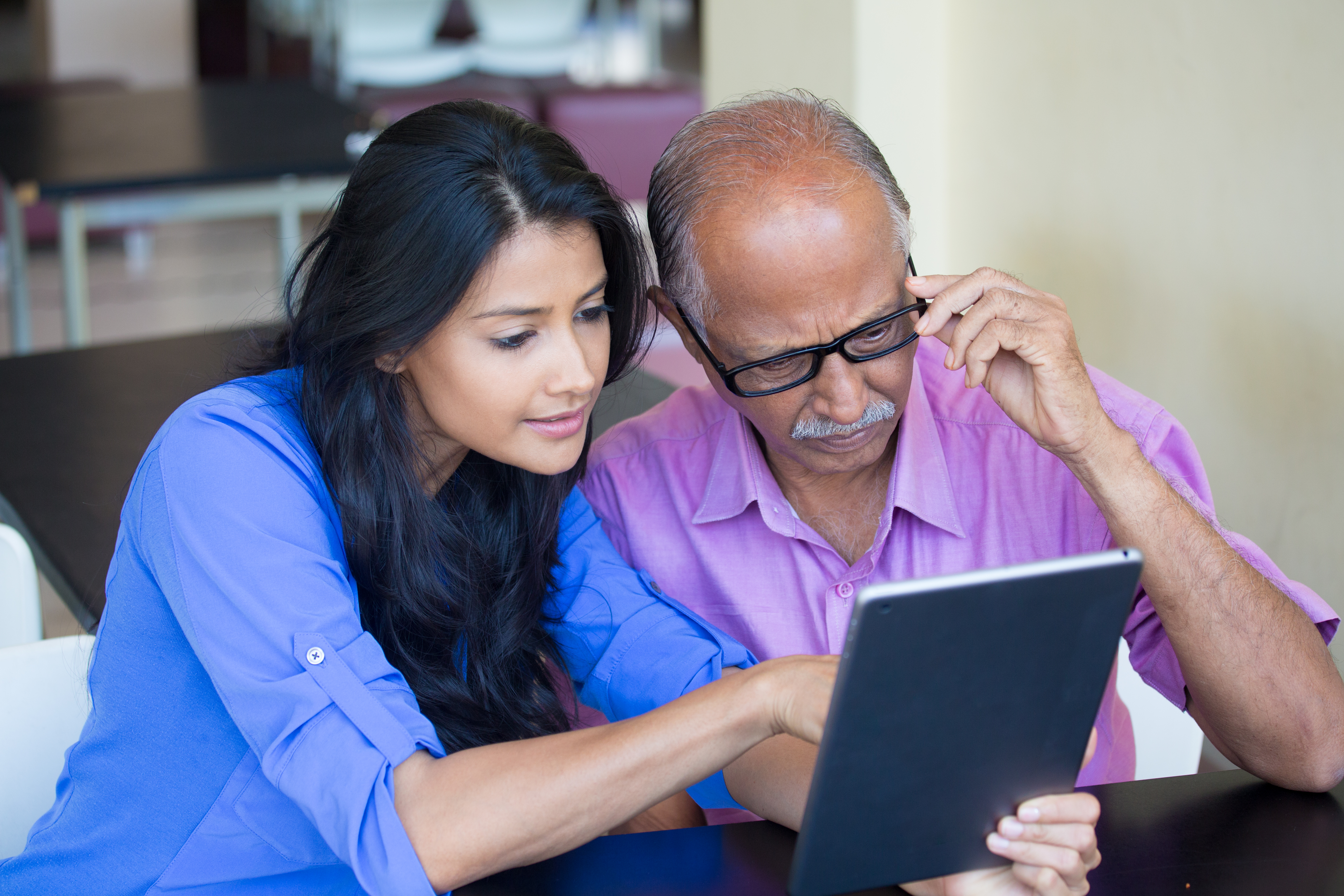 A young woman is pointing at a tablet screen while an older man is watching closely.