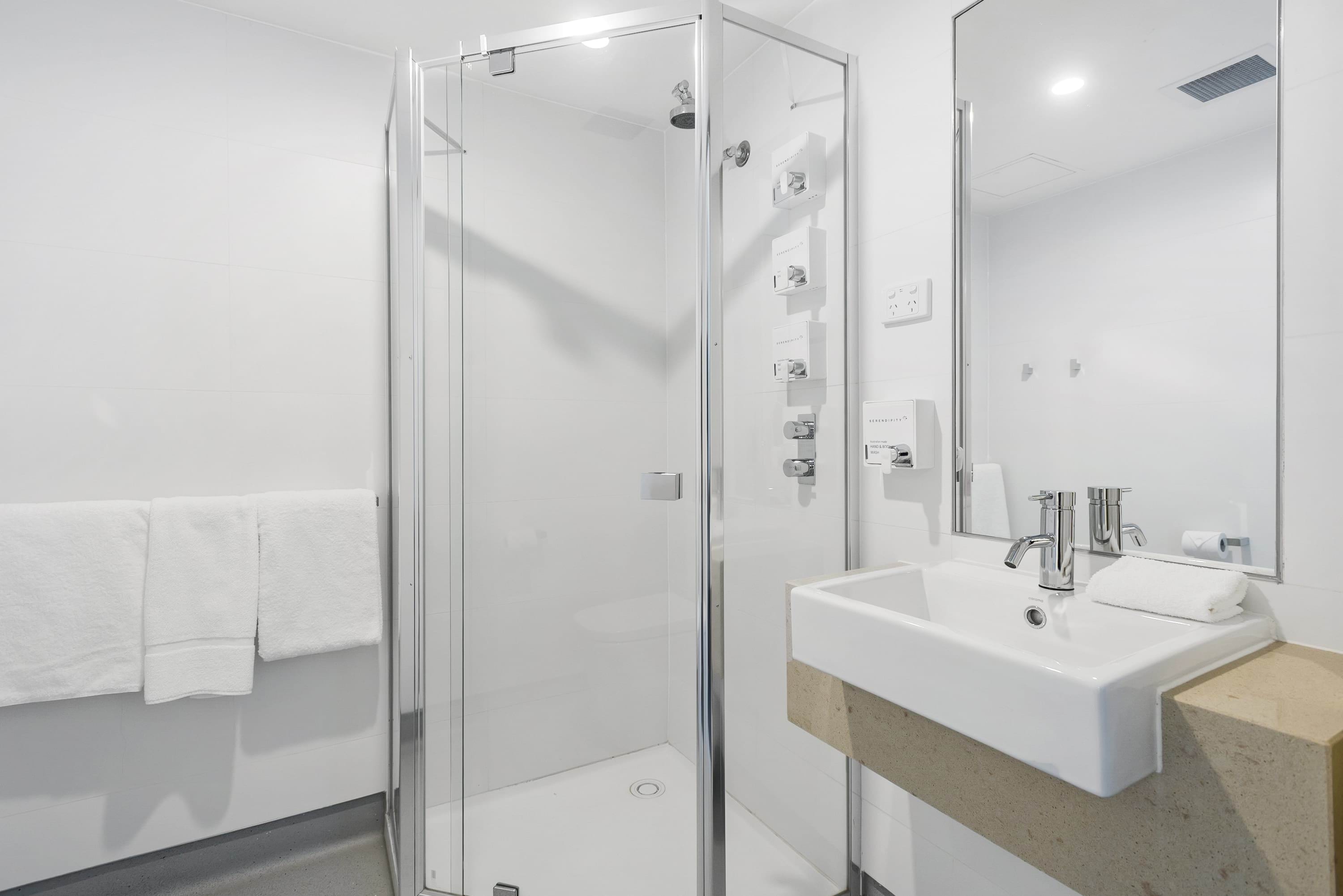 Image shows the VEMI accommodation bathroom with shower, skink, mirror and towels..