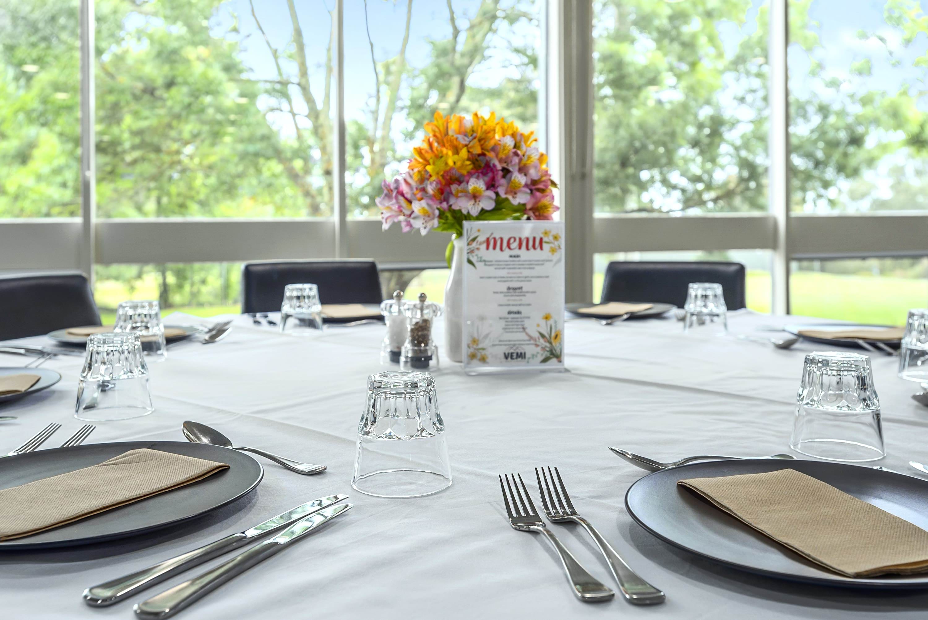 Image shows a table set with plates and cutlery on a white tablecloth and flowers at the centre.