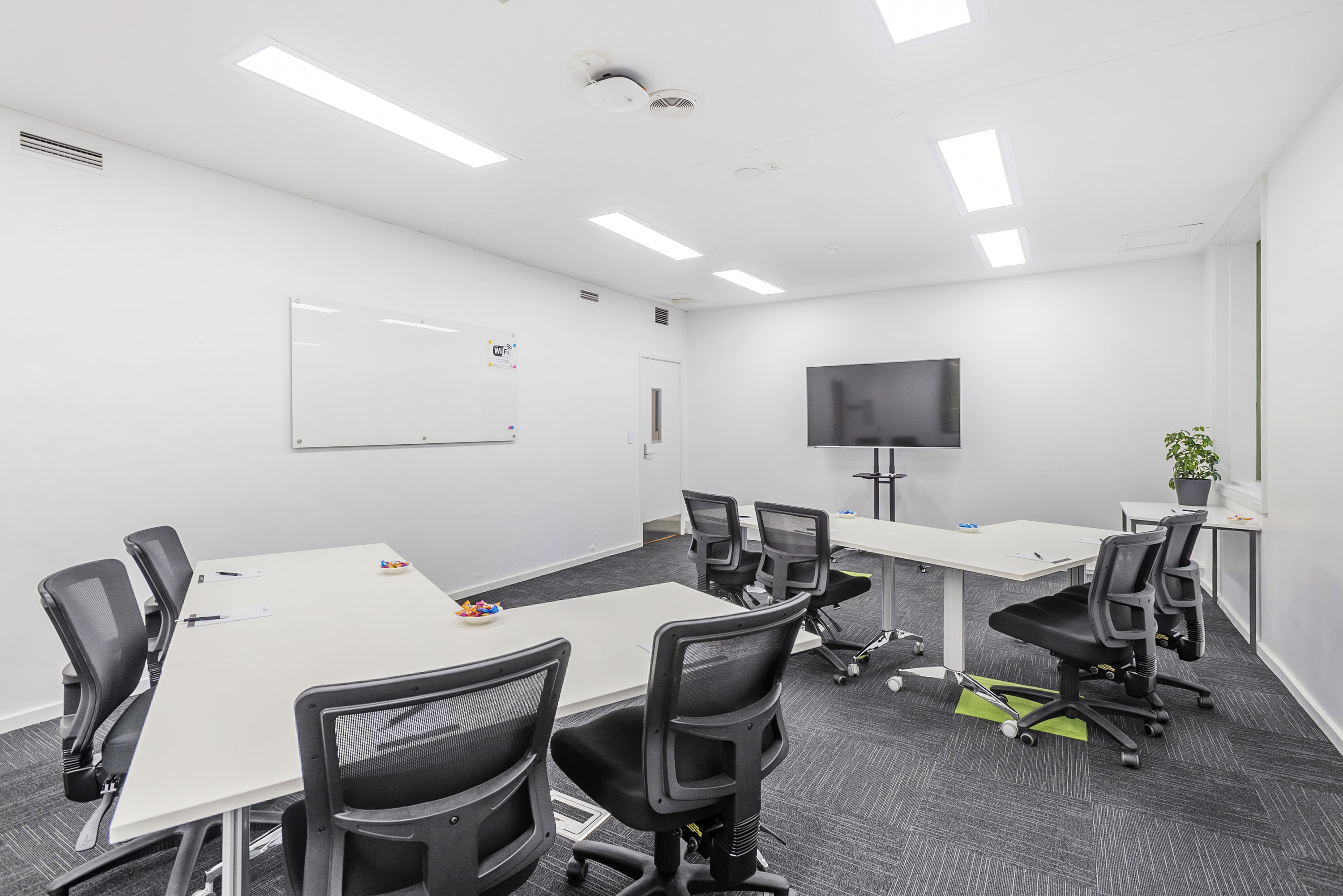 Image shows one of the Syndicate meeting rooms at the VEMI Conference Centre with a screen, tables and chairs.