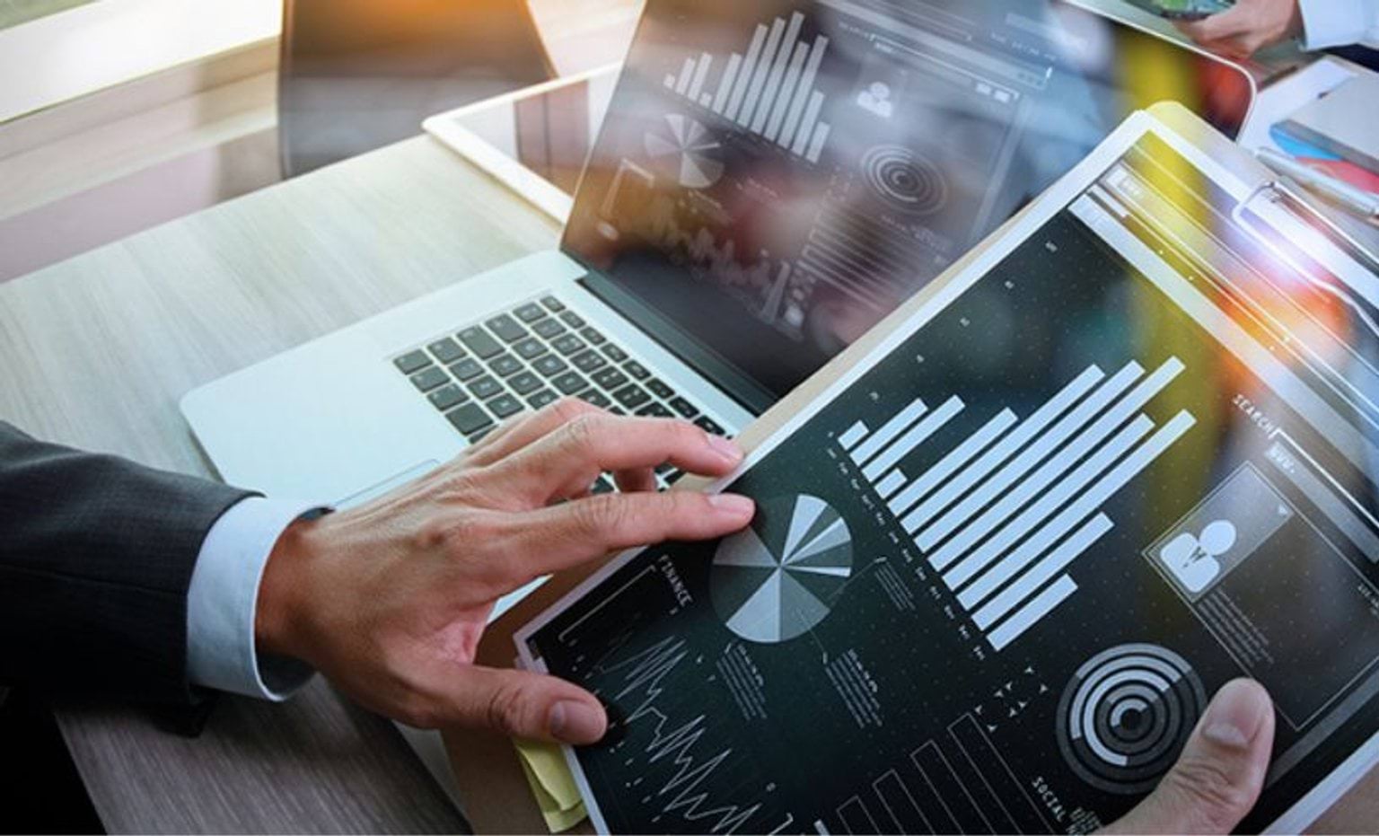 Person using laptop and tablet looking at charts and graphs Person using laptop and tablet looking at charts and graphs