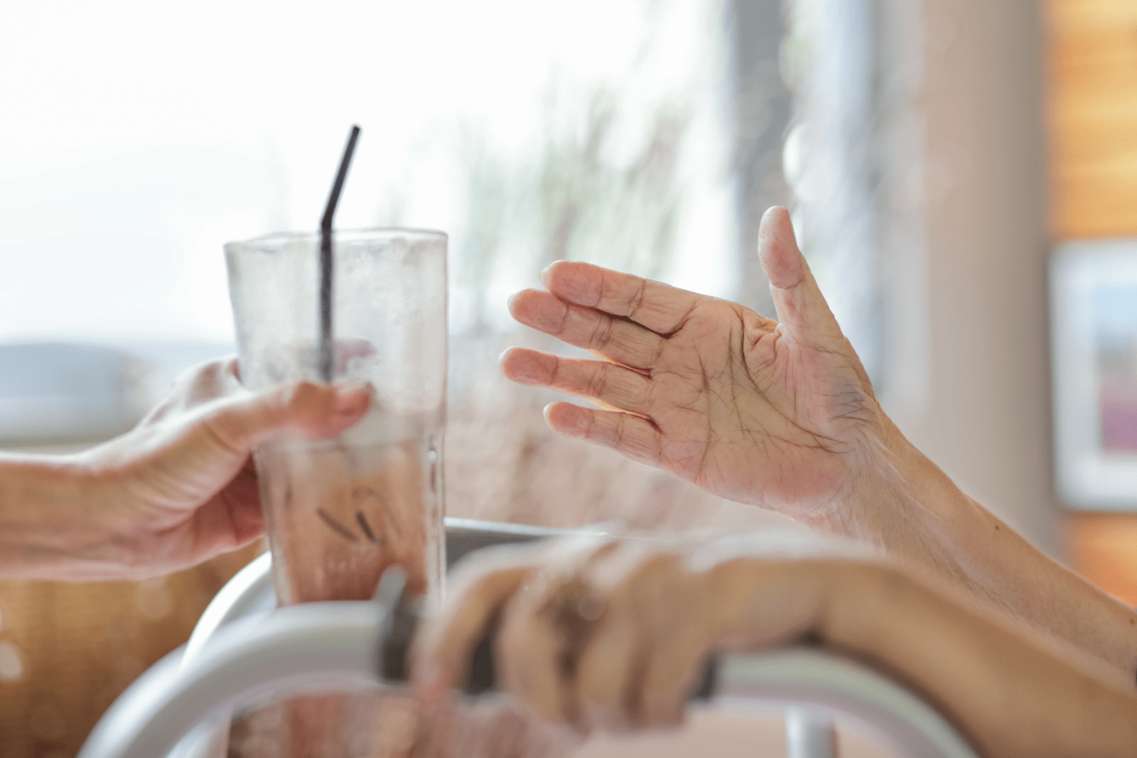 A glass with a beverage and black straw in it being handed to another person with their hand outstreched 