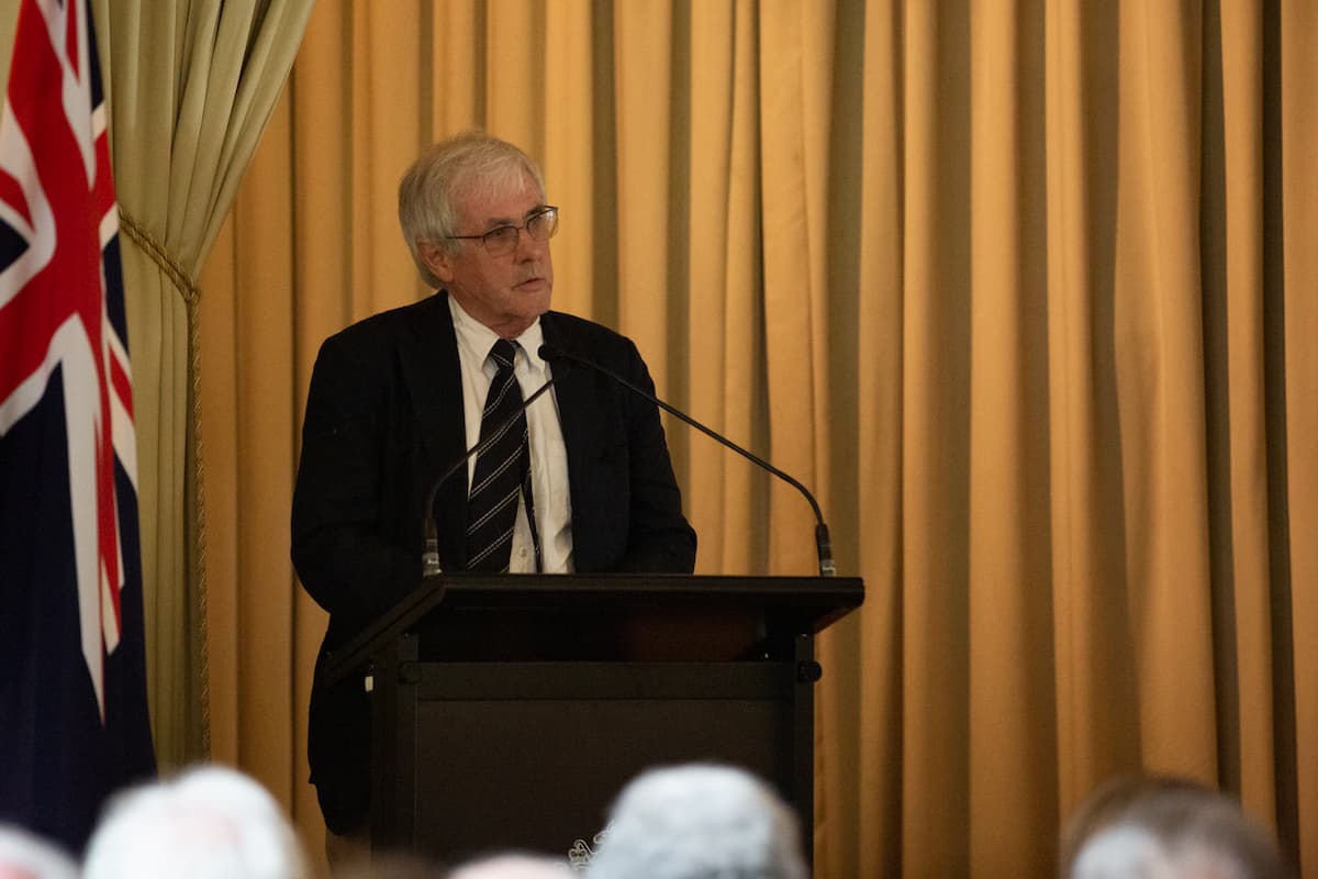 Don Watson speaks from the lectern, the Australian flag is behind his right shoulder