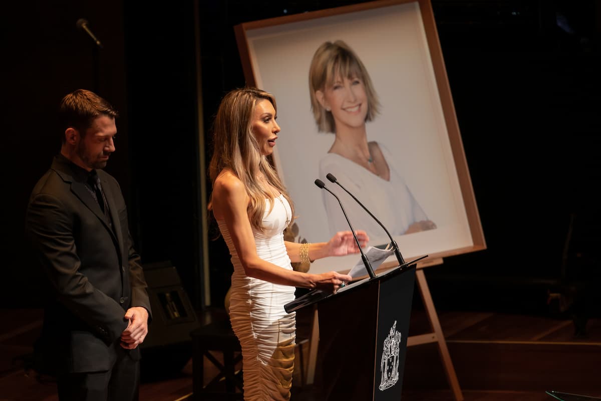 A woman stands at a podium speaking into a microphone. 