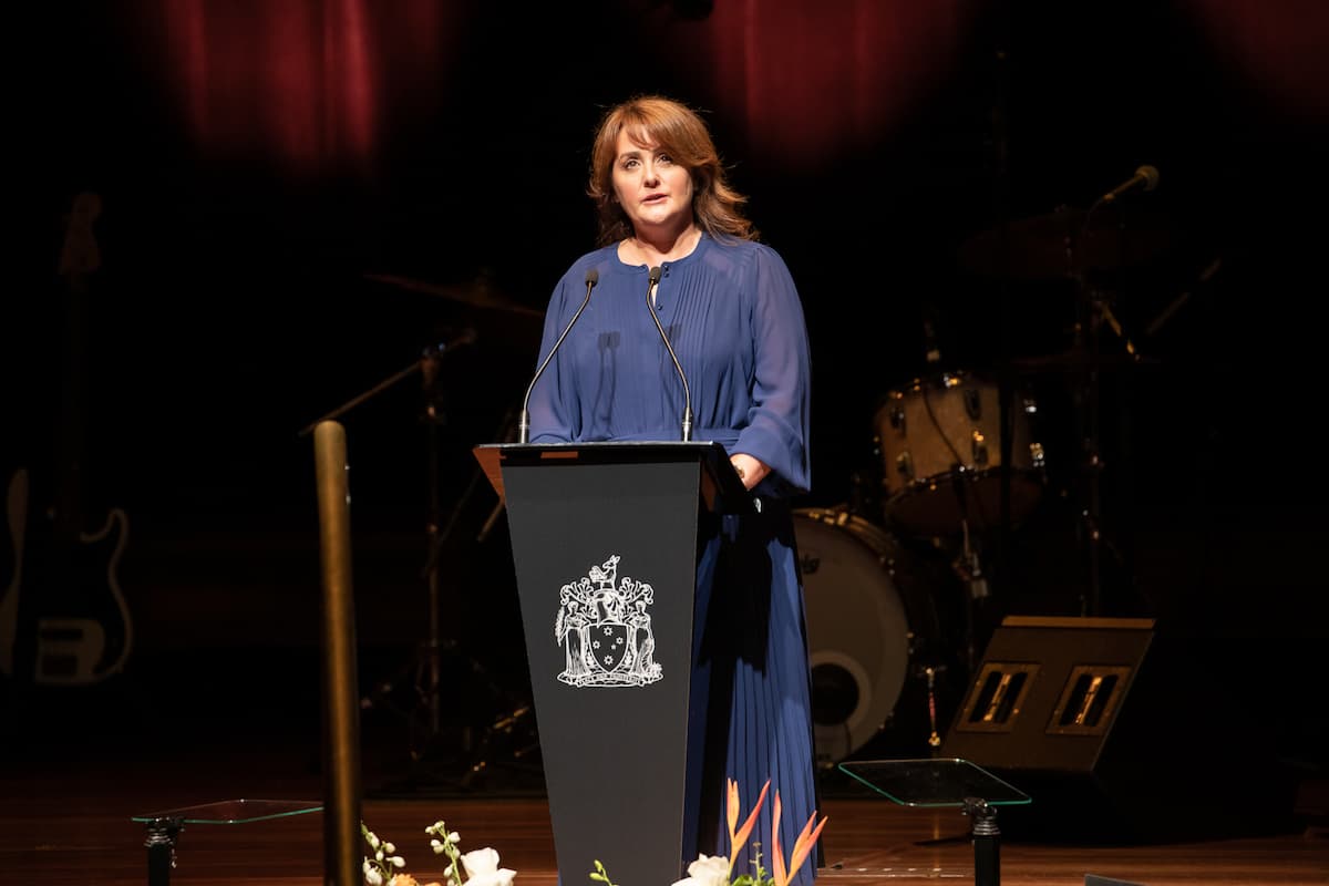 A woman in a navy blue dress speaks at a podium on stage