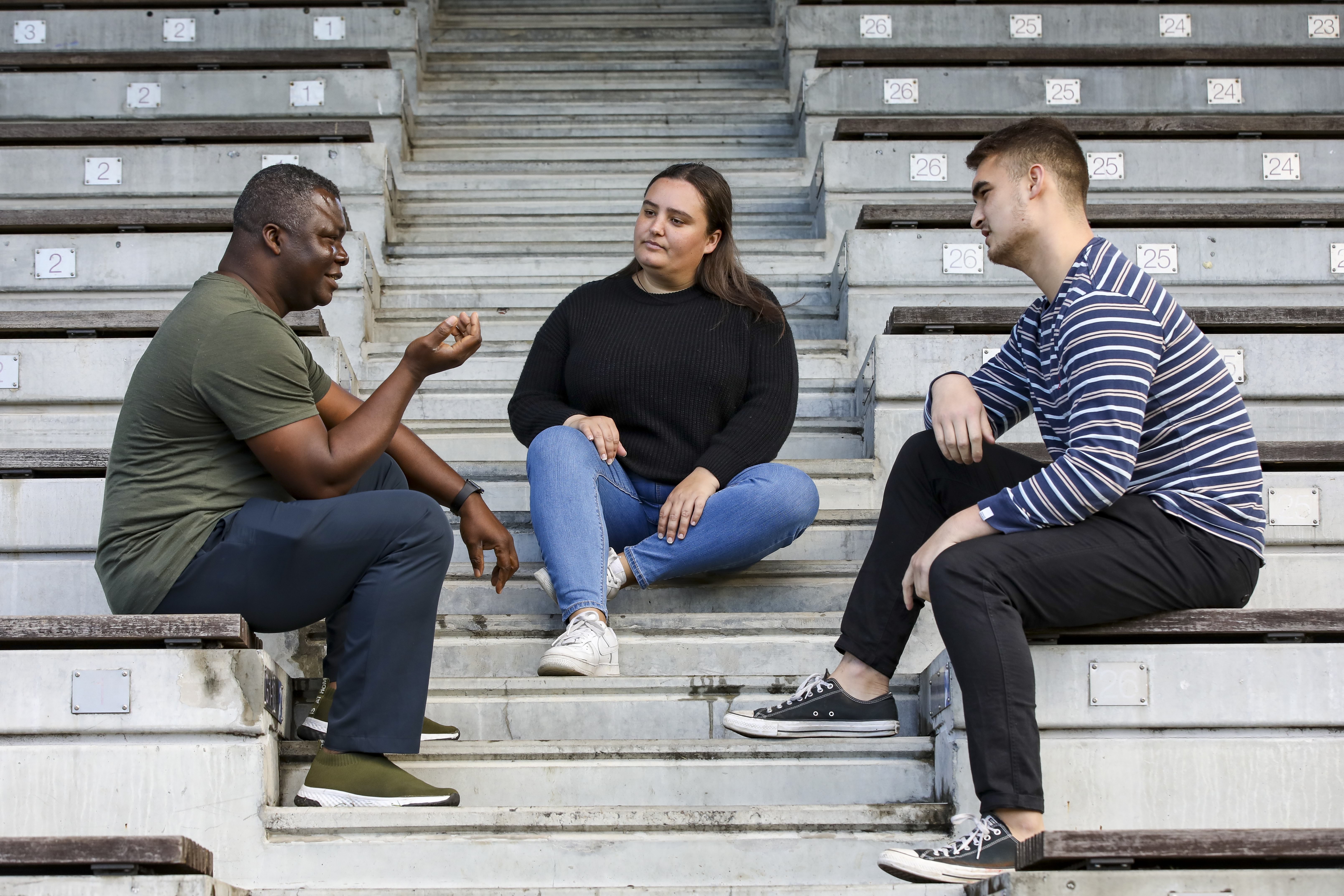 Three people have a conversation while sitting on bleachers and steps