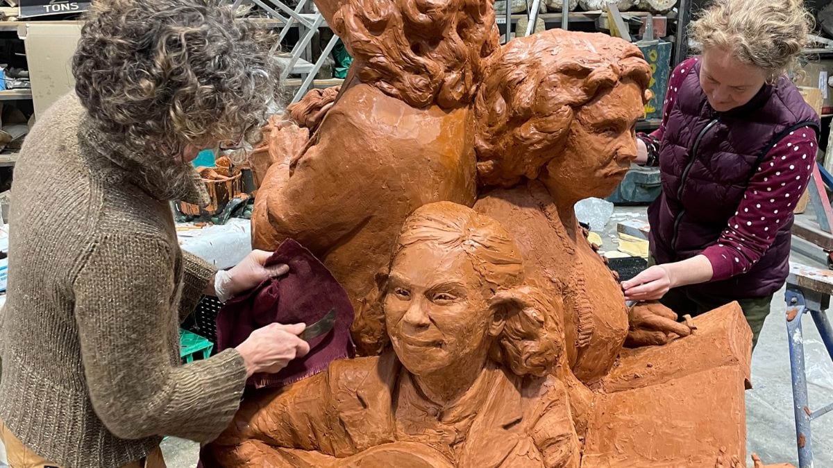 The artists add details to the clay sculpture using sculpting tools and their hands.