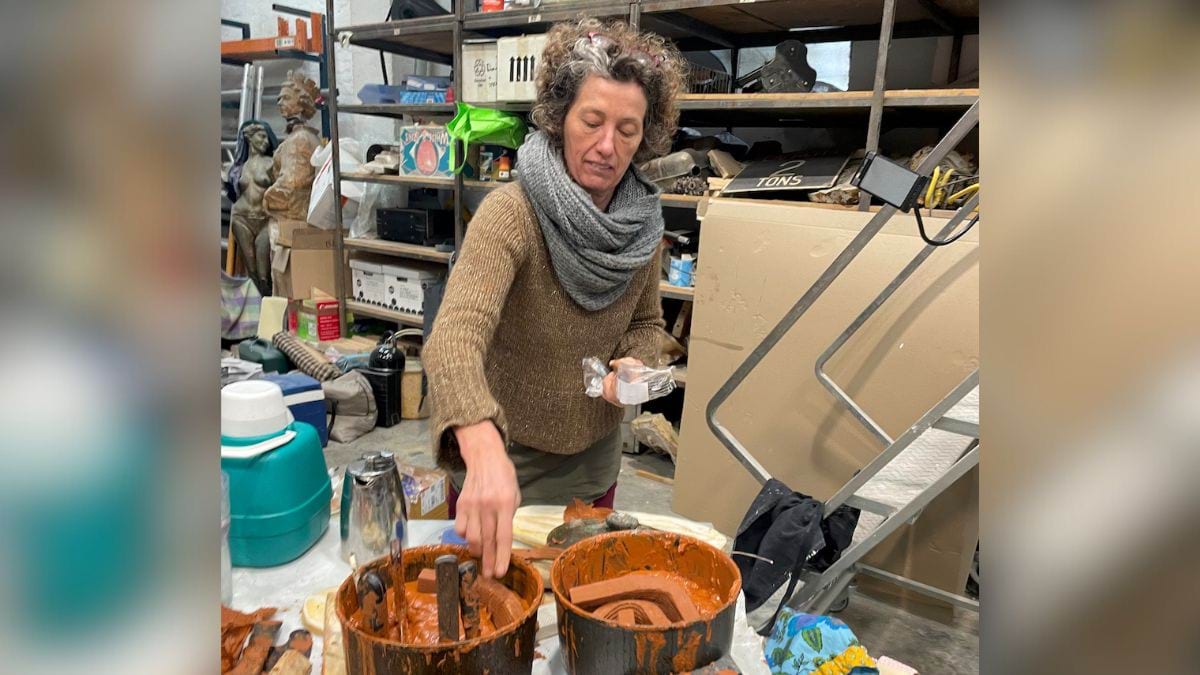 Artist Jessie McLennan is in the workshop stirring clay in a pot.