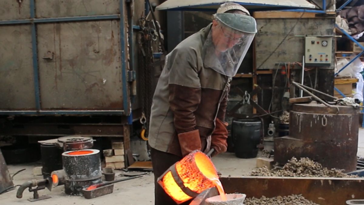 Cameron is wearing protective gear as he pour molten bronzed into a mould at the foundry.