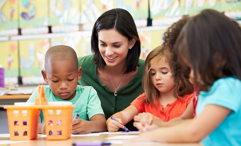 A teacher sitting with some students in a classroom.