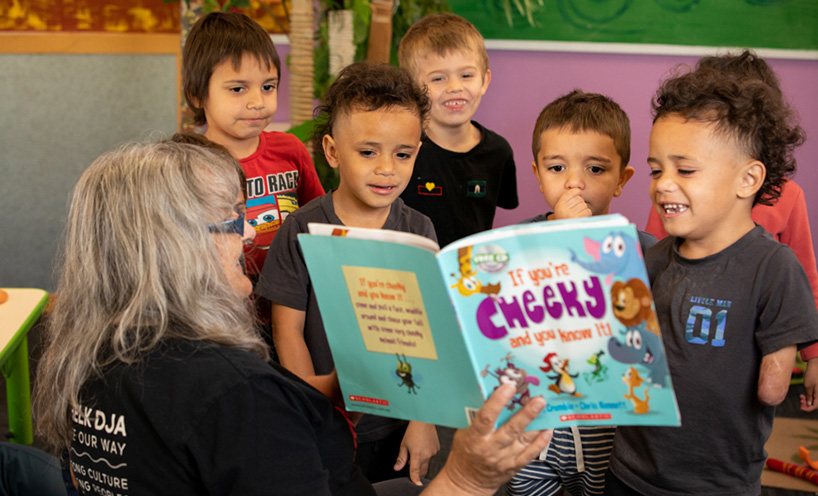 A teacher showing a book to a group of kids in a classroom