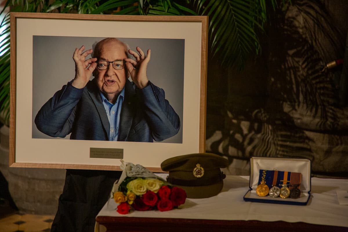 A portrait of Father Bob sits next to his army hat, medals and flowers on a table.