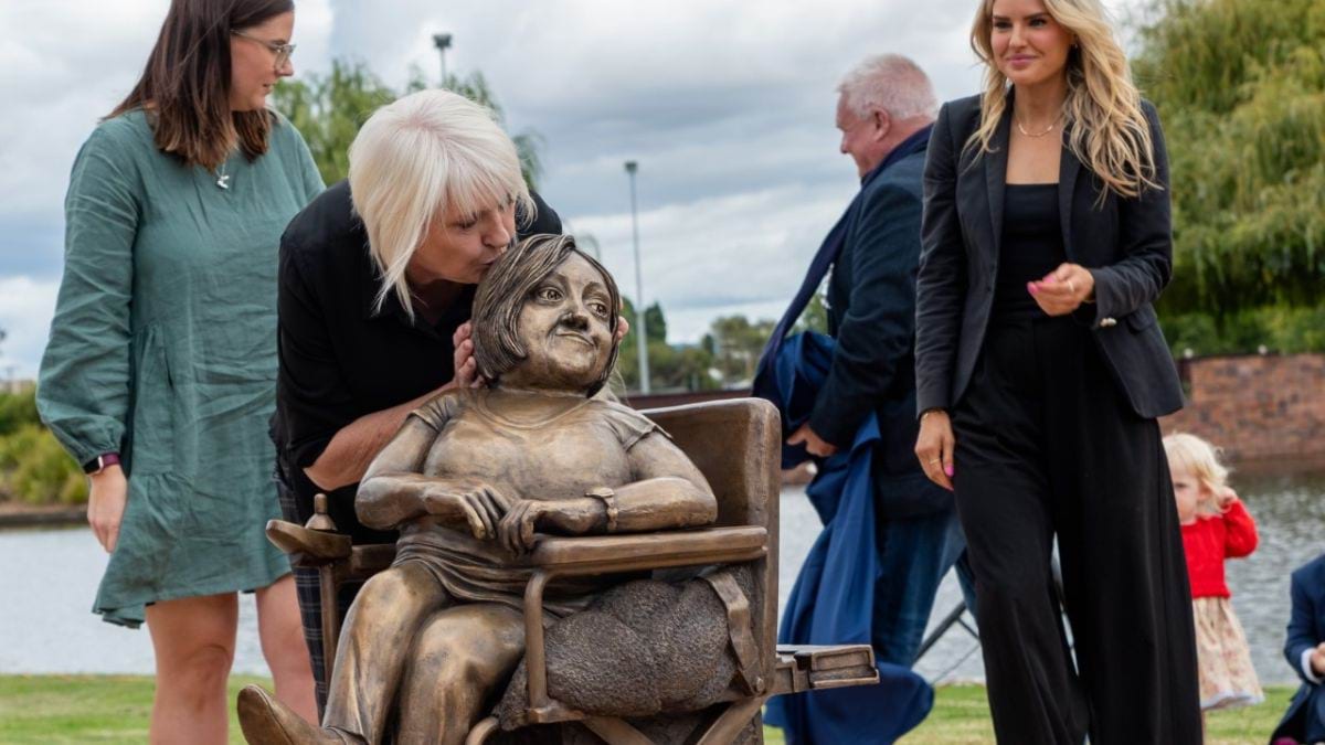 The Remembering Stella Young statue is unveiled. Lynne, Stella's Mum, kisses the head of the statue, as the Young family is gathered behind.