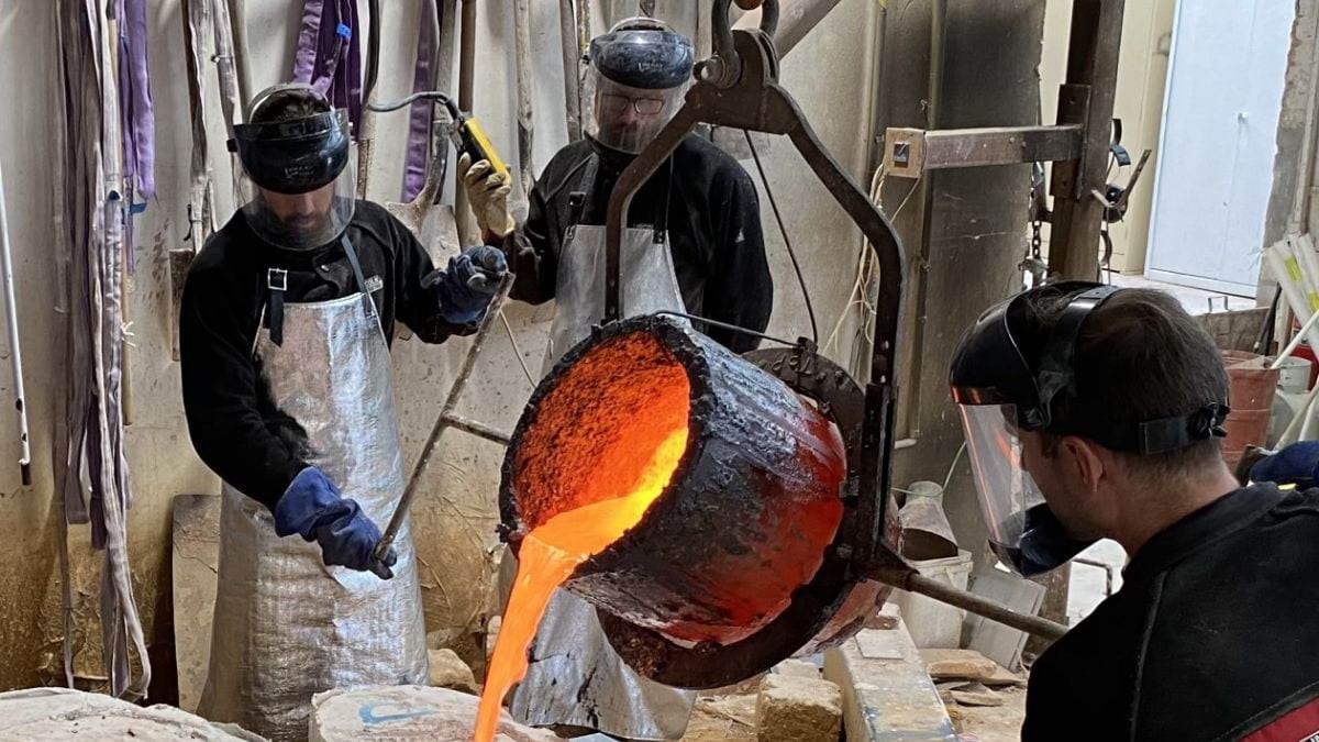 At the foundry, molten bronze is poured very carefully in to the moulds. The three artisans are clad in protective gear including aprons, gloves and visors.