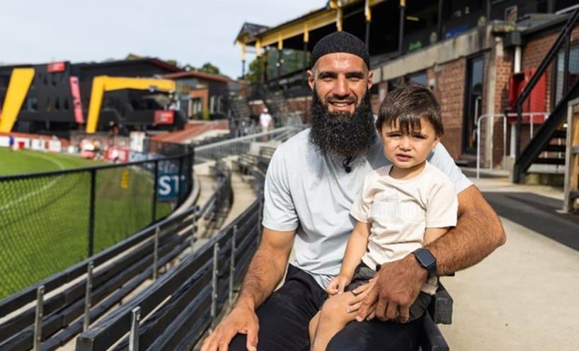 A young child seated on former AFL player Bachar Houli's lap.