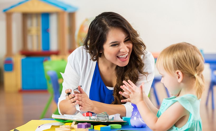 An early childhood teacher is sitting with a student in a classroom are laughing together.