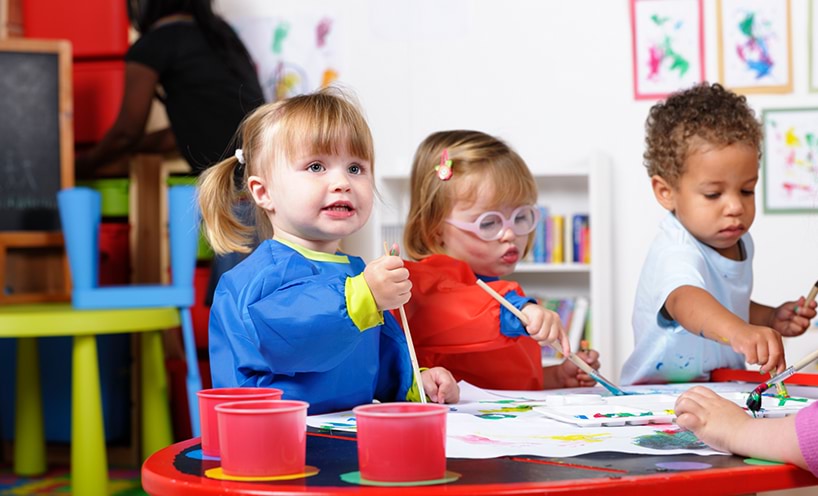 A group of kids sitting around a table drawing and painting together.