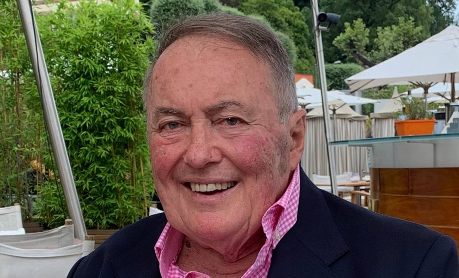 The Honourable Thomas Roper Tom smiles at the camera, he wears a pink plaid shirt with a blue blazer.