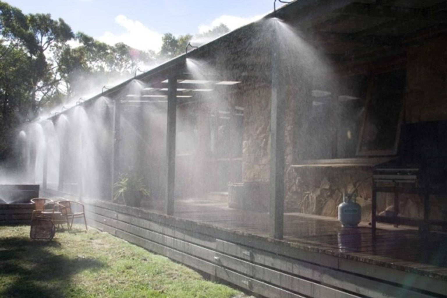 Image shows water spraying from piping around a veranda of a house in bushland