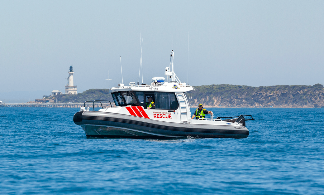 Image shows a boat on the water, with a lighthouse in the background