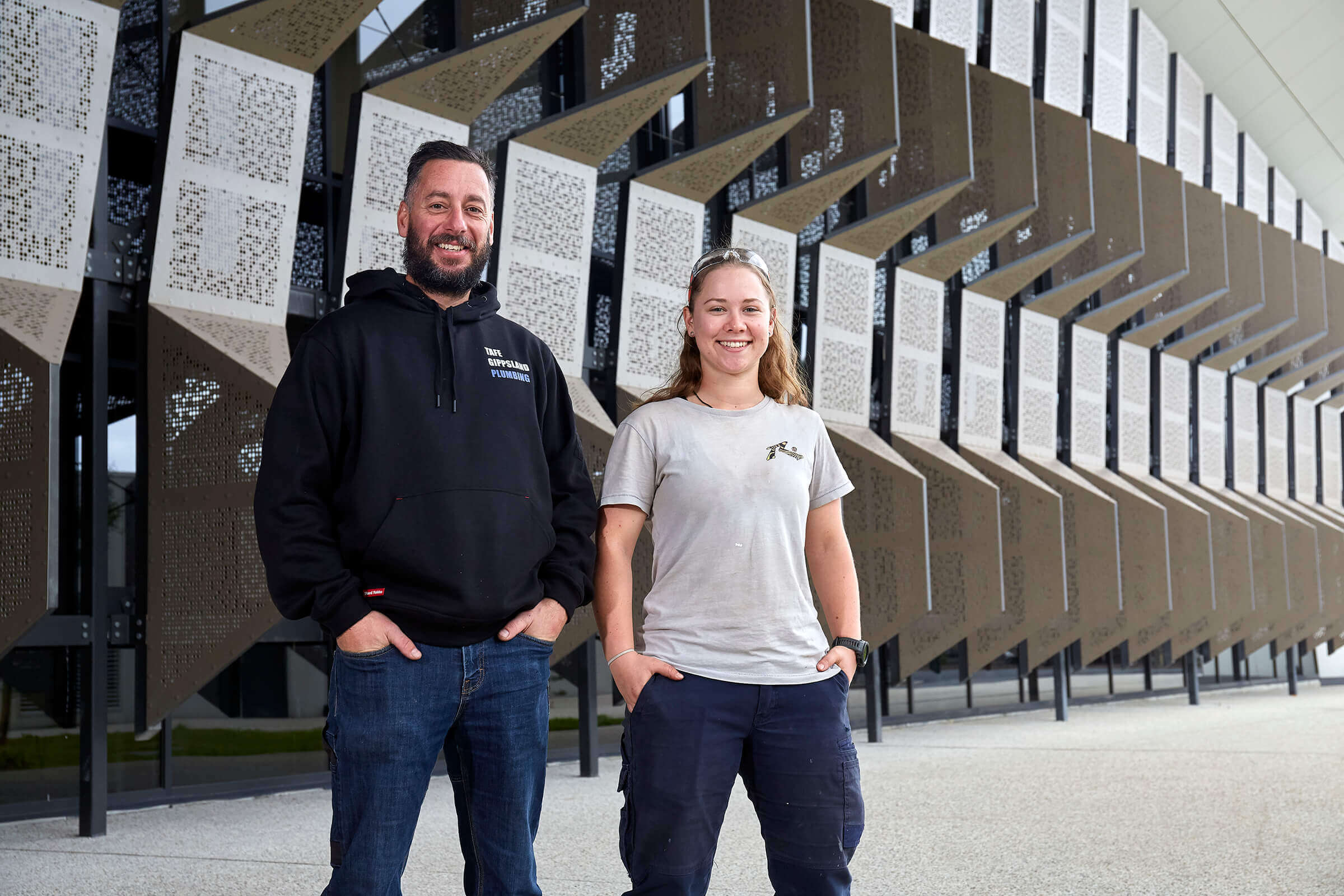 Man and woman with hands in pockets standing in front of Gippsland TAFE Trades Centre.