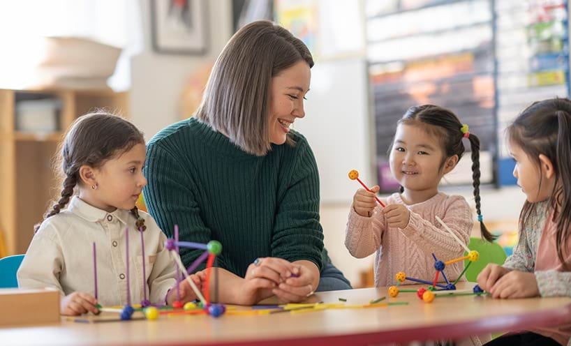 Decorative image of female early childhood educator sitting at a table with three children.