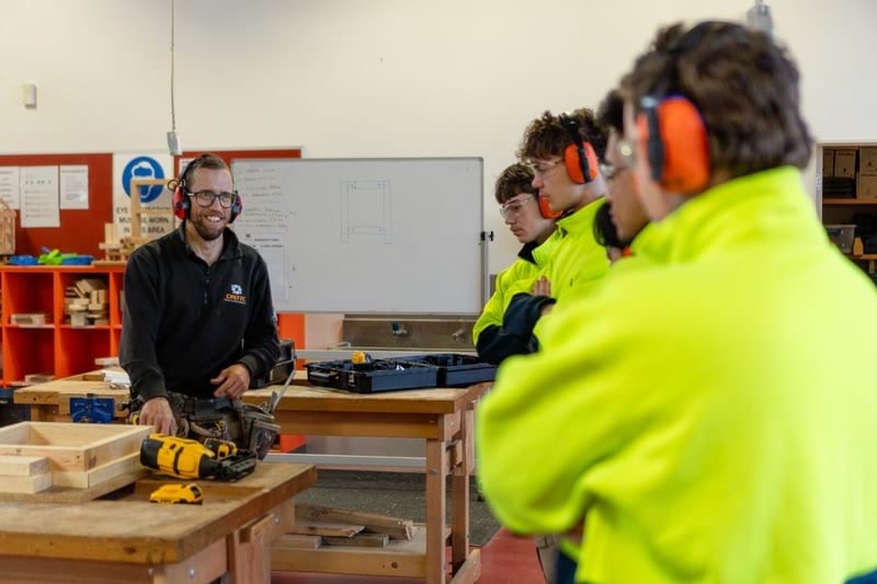 2023 Victorian Training Awards Teacher or Trainer of the Year winner Thomas Patterson in teaching workshop with trade students holding a power drill, wearing safety goggles and hearing protection