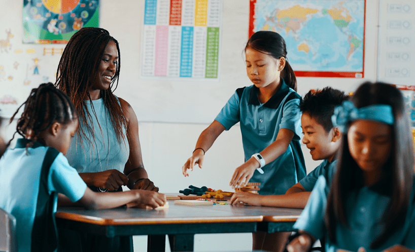 Teacher sitting at a desk with primary school aged children around her