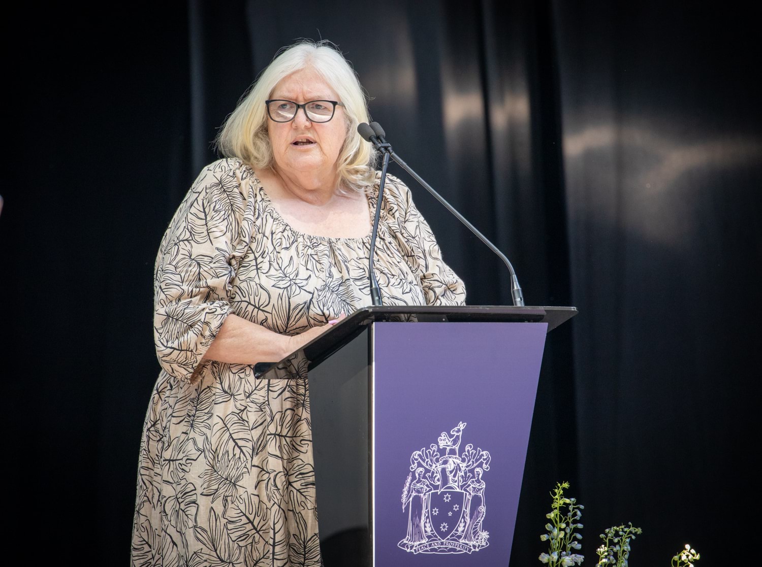 a woman in a patterned dress stands at a podium speaking to an audience  