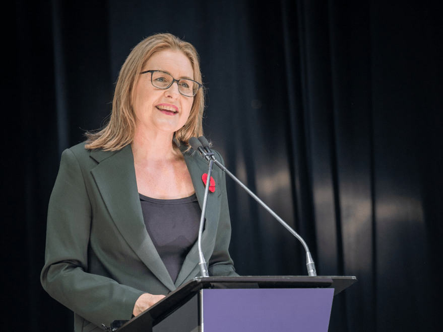 a woman in a dark green suit stands at a podium speaking to an audience