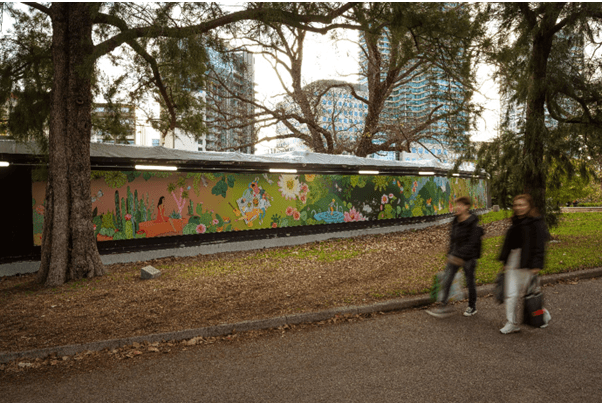 Two people walking in front of the Gathering in the Gradens mural