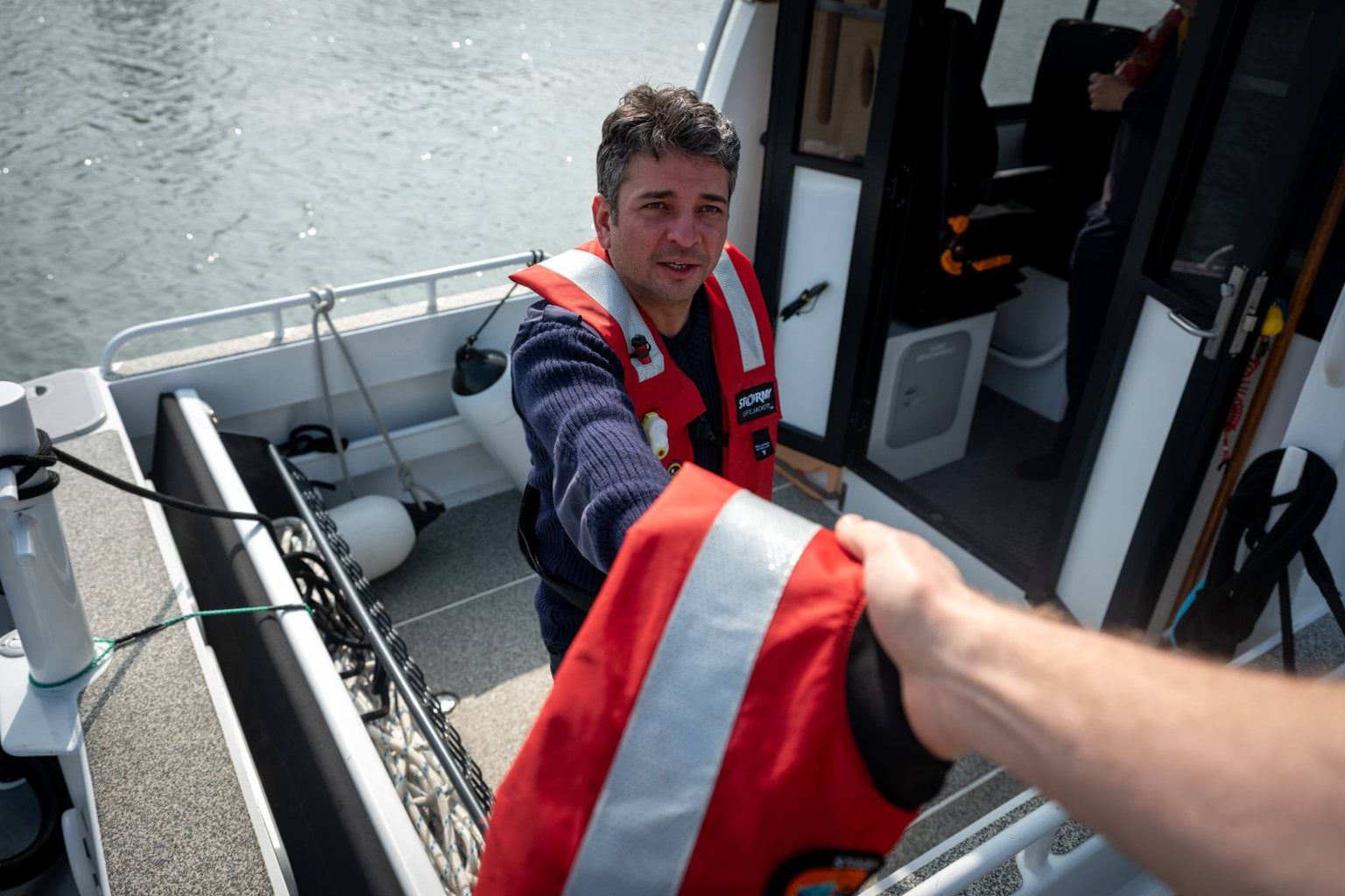 Image shows a MSAR crew member on a boat, handing a life jacket to someone.