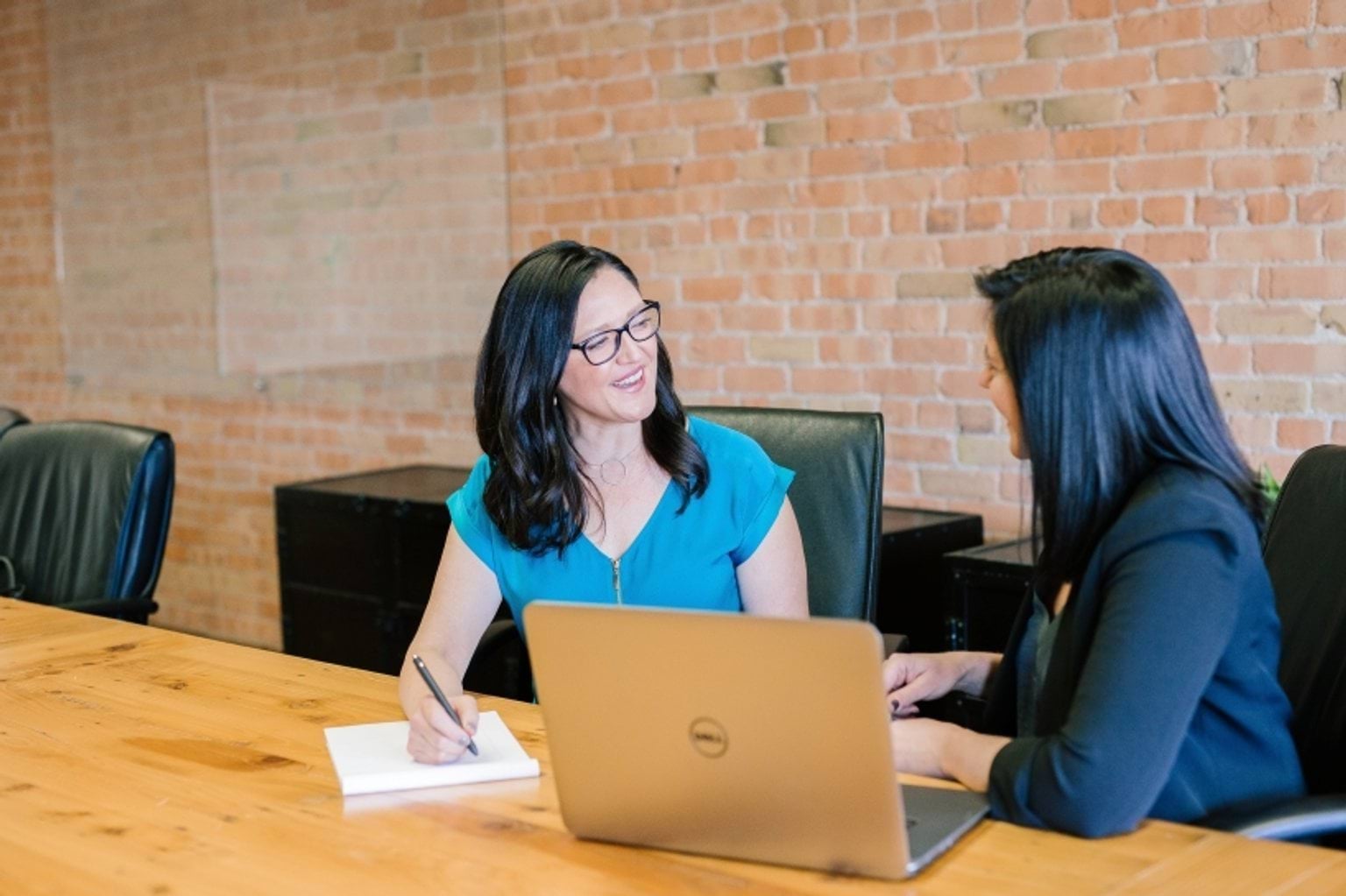 Two people at a meeting room table with a laptop in front of them.